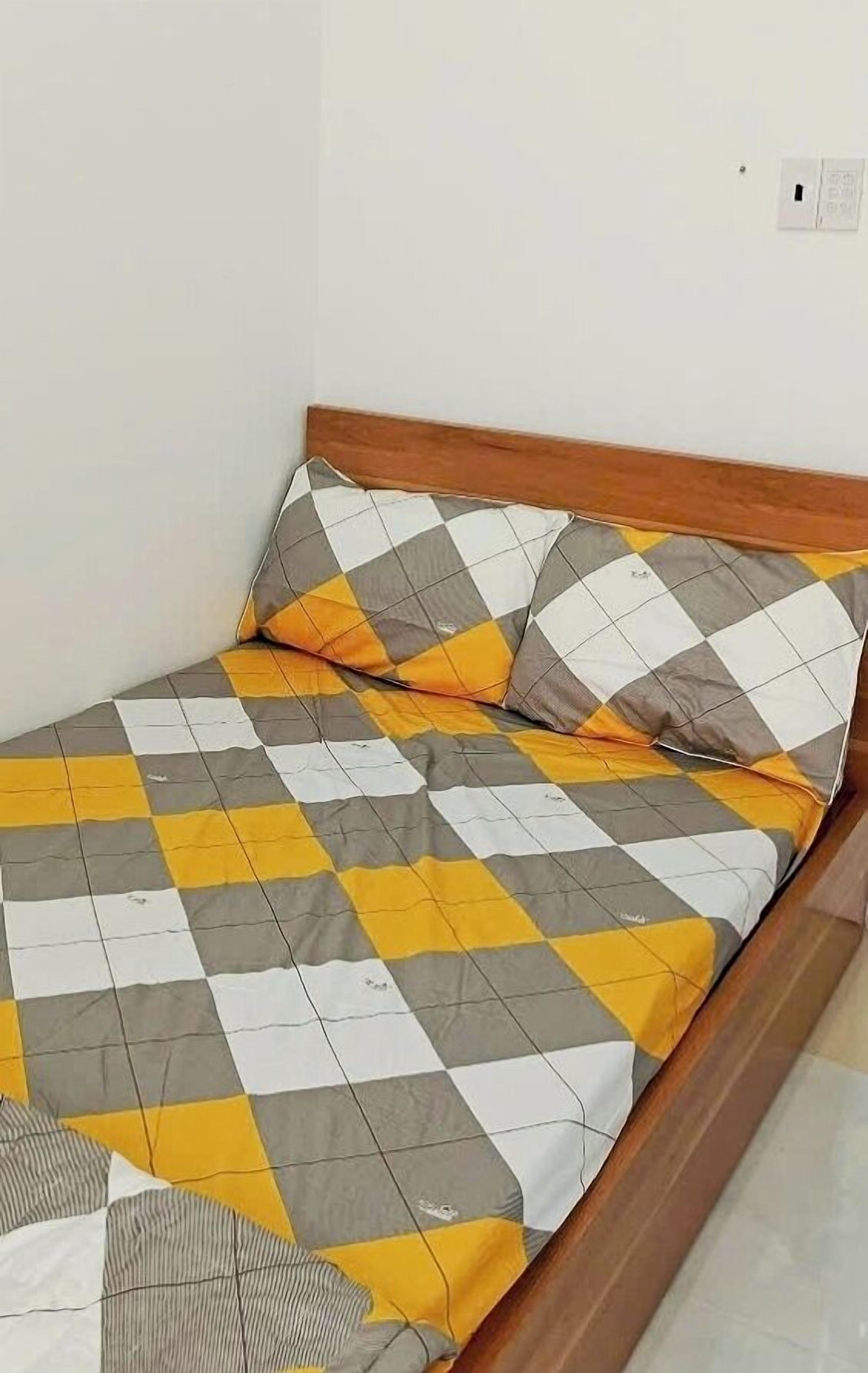 A bed with a checkered bedspread in yellow and gray, and a wooden headboard.