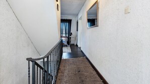 A narrow hallway with a black railing, a textured wall, a hanging light fixture, and a window with curtains. - Holiday Home 'Am Sallingbach' with Balcony and Wi-Fi (Sallingberg)