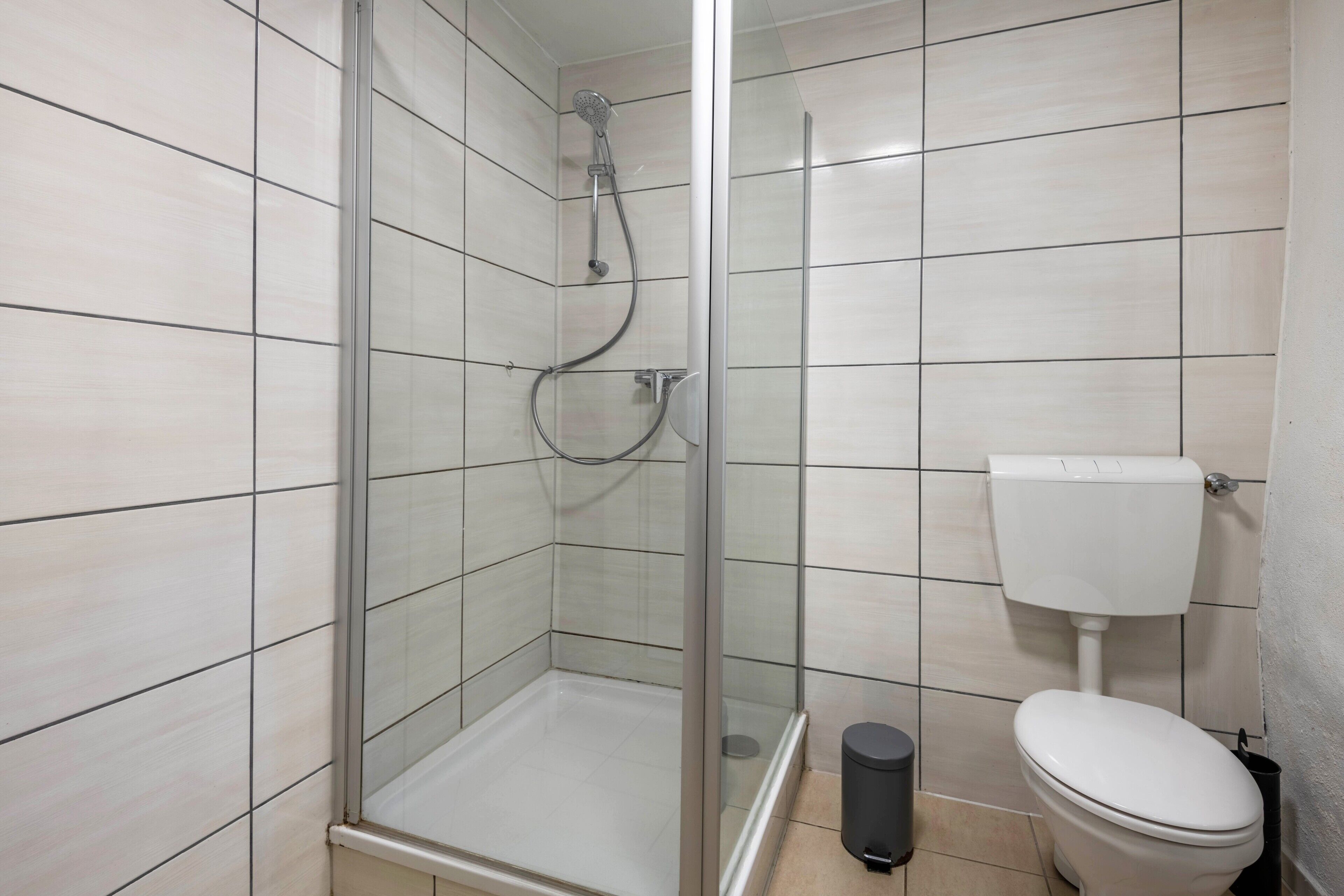 Een badkamer met een douchecabine van glas, een toilet en een prullenbak.