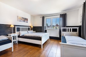 Une chambre avec deux lits, une fenêtre avec des rideaux, un radiateur et un tableau au mur.