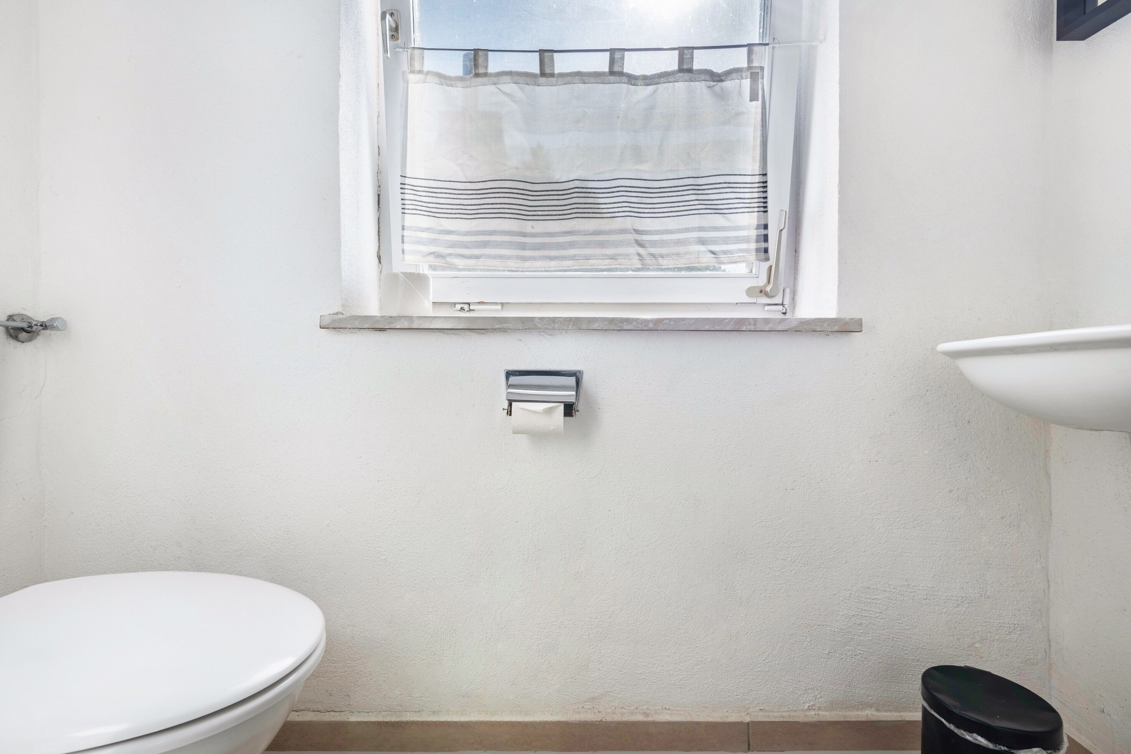 A bathroom with a toilet, a sink, and a window with a striped curtain.