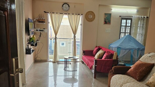 Ein Wohnzimmer mit einem roten Sofa, einem kleinen runden Tisch mit einer Pflanze, einem Deckenventilator und Blick ins Freie durch große Fenster.