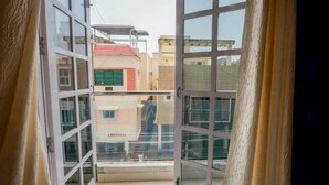 Blick vom Balkon mit Glastür auf ein Wohngebiet mit Gebäuden und einem Geschäft namens "ARHINASA".
