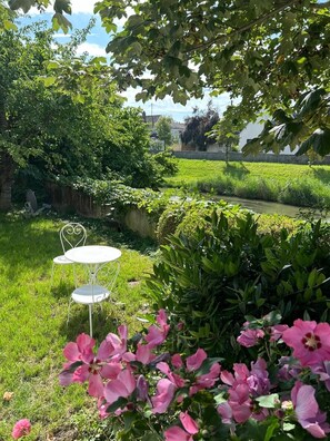 Un jardin avec une table et des chaises en métal, un bassin et des fleurs roses.