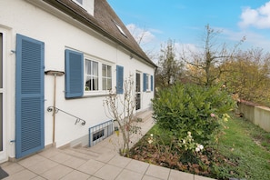 Un bâtiment blanc avec des volets bleus, un petit jardin et un ciel dégagé.
