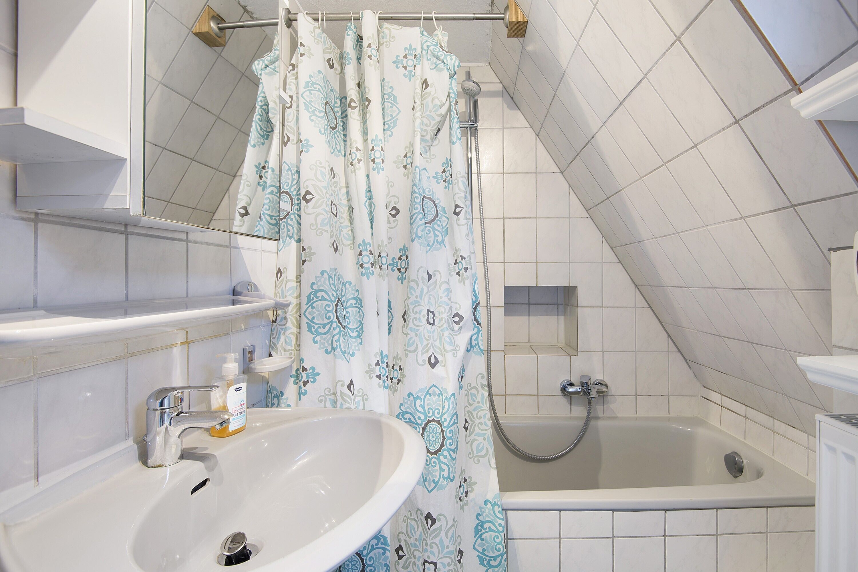 A bathroom with a sink, shower, and a patterned shower curtain.