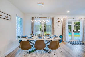 A dining area with a table set for six, a chandelier, and a view of a pool through glass doors.