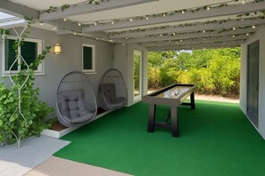 An outdoor patio with two hanging chairs, a pool table, and a green artificial turf floor.