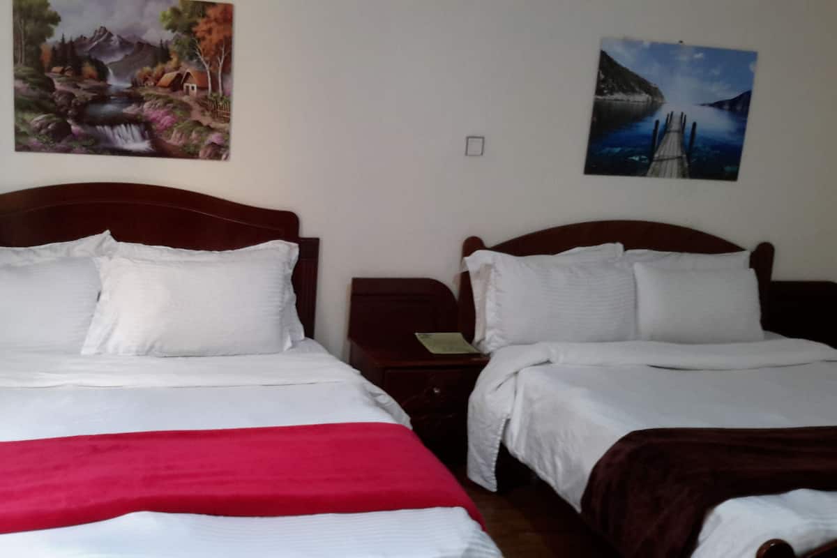 A hotel room with two beds, a nightstand, and two wall-mounted paintings.