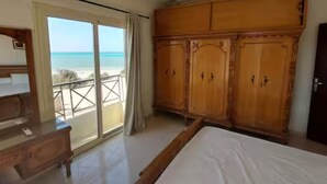 Ein Schlafzimmer mit einem großen Bett, einem Holzschrank und einem Balkon mit Blick auf den Strand.