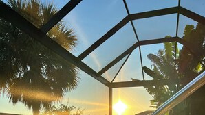 Una piscina con vista despejada al atardecer, rodeada de palmeras y una baranda metálica.