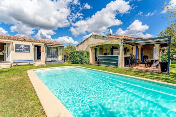 Una piscina con zona de patio, un edificio con un letrero y un cielo azul despejado.