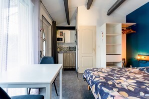 Una habitación pequeña con cama, escritorio y kitchenette.