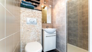 A bathroom with a toilet, sink, mirror, and shower area. - Studio 'Luberon' with Mountain View, Wi-Fi and Air Conditioning (Taillades)