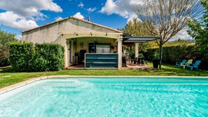 A swimming pool with a covered patio area, a building with a garage door, and a tree in the background. - Studio 'Luberon' with Mountain View, Wi-Fi and Air Conditioning (Taillades)