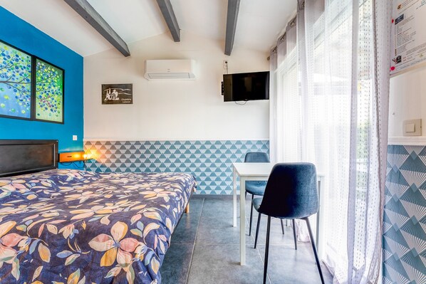 A room with a bed, a desk, a chair, an air conditioner, a TV, and a window with curtains. - Studio 'Luberon' with Mountain View, Wi-Fi and Air Conditioning (Taillades)