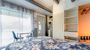 A bedroom with a bed, a desk, chairs, a wardrobe, and a window with curtains. - Studio 'Luberon' with Mountain View, Wi-Fi and Air Conditioning (Taillades)