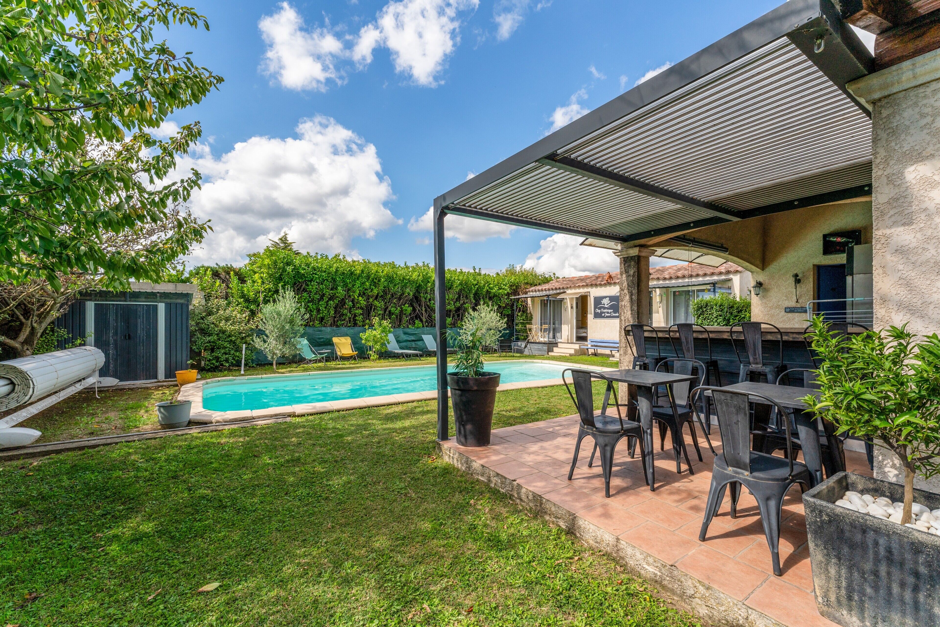 Un espacio exterior cubierto con piscina, mobiliario de patio y vista a una casa al fondo.