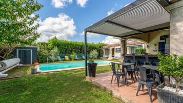 Un espacio exterior cubierto con piscina, mobiliario de patio y vista a una casa al fondo.