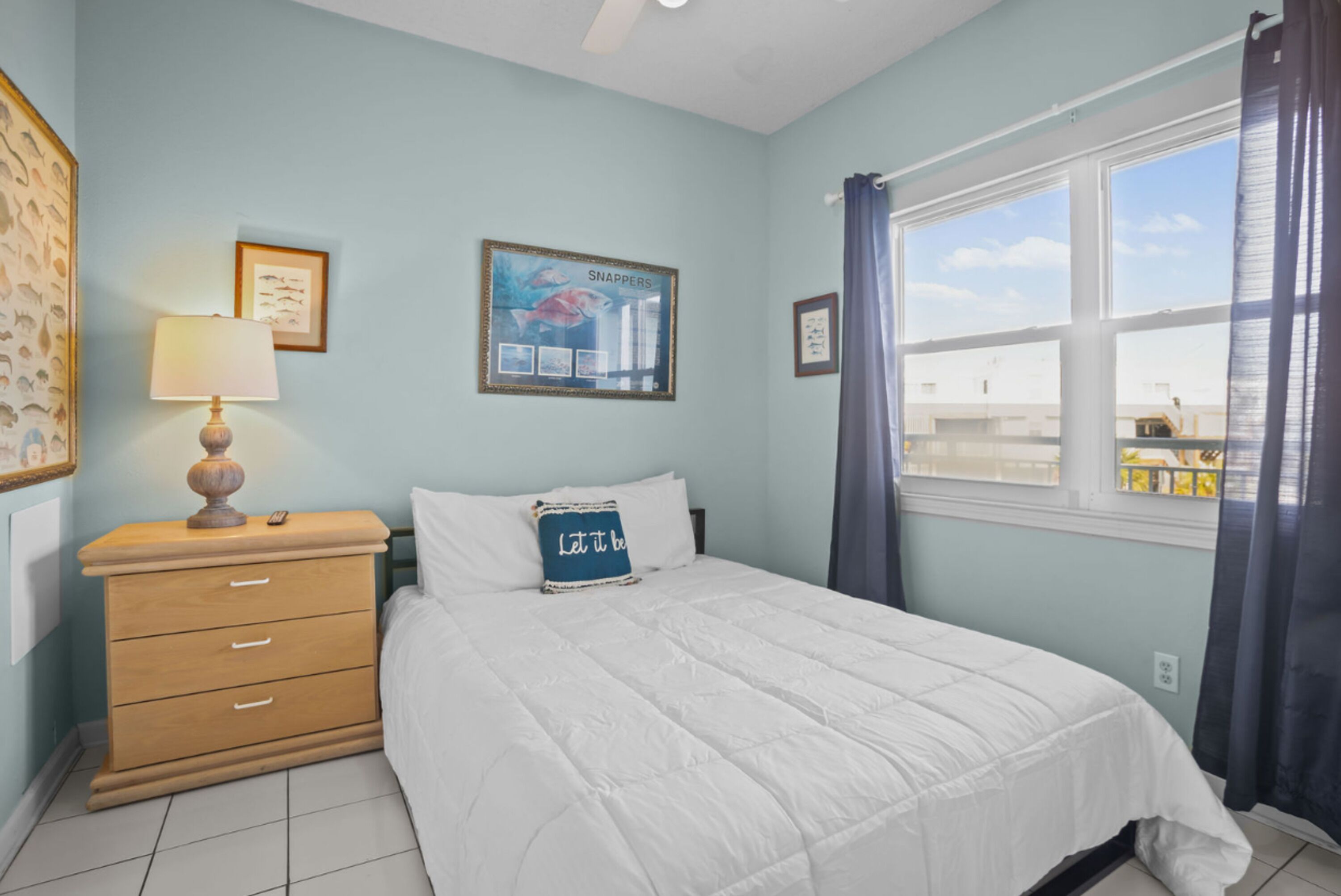 Un dormitorio con cama, mesita de noche, lámpara y ventana con cortinas.