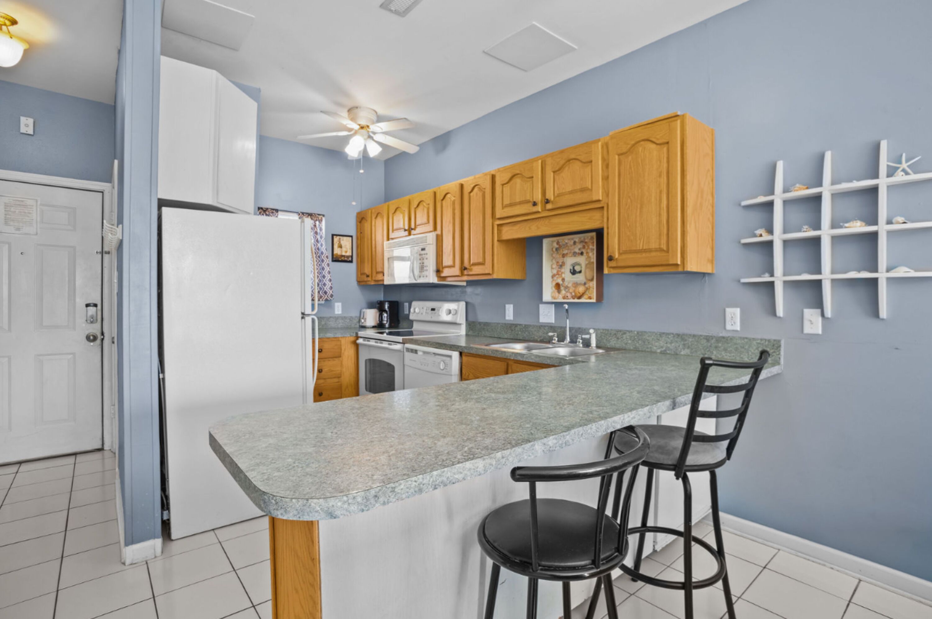 A kitchen with a granite countertop, wooden cabinets, a refrigerator, a microwave, a stove, and a ceiling fan.