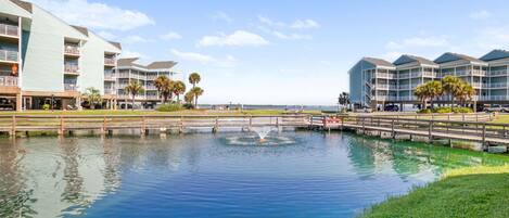 A waterfront hotel with multiple balconies, a small bridge, and a fountain.