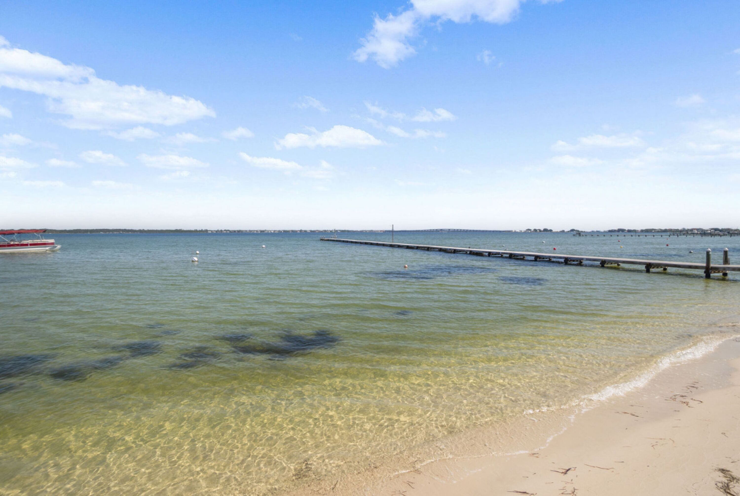 Una spiaggia con acque cristalline, un molo che si protende verso il mare e una barca ormeggiata vicino alla riva.