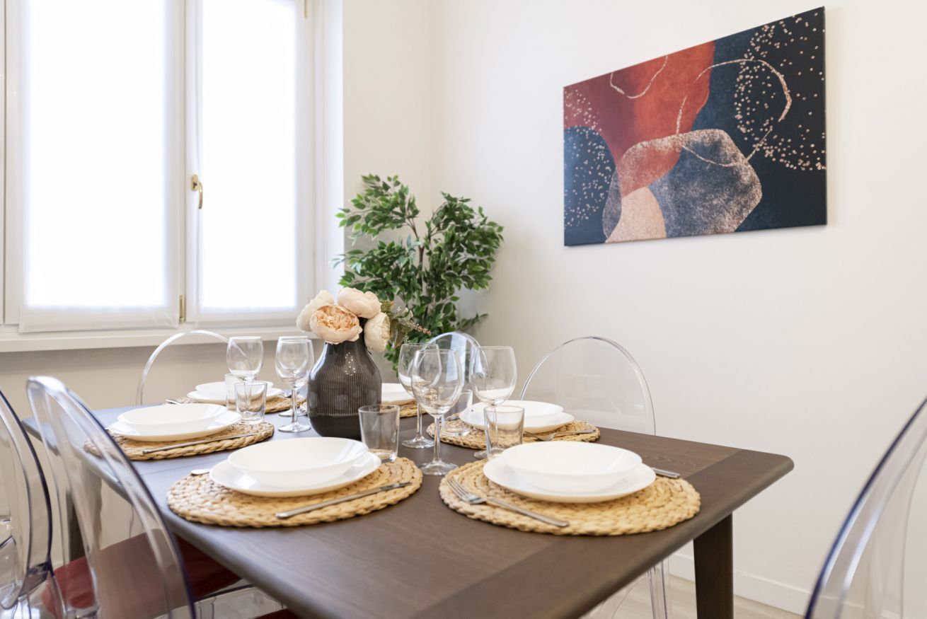 A dining table set with plates, glasses, and a vase with flowers.