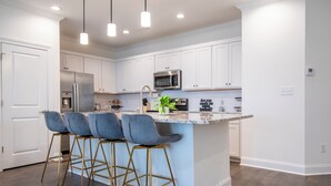 A modern kitchen with white cabinetry, a stainless steel refrigerator, a microwave, and a bar area with stools. - Family-Friendly 3BR Condo Sleeps 9, Ensuite Bathrooms (Oxford)