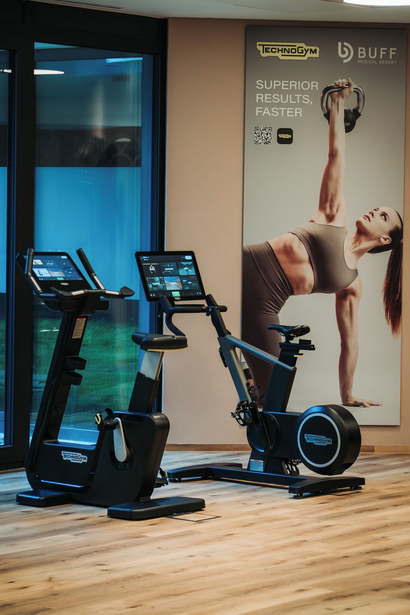 Un gimnasio con máquinas de cardio, una pesa rusa y un cartel publicitario que anuncia resultados superiores.