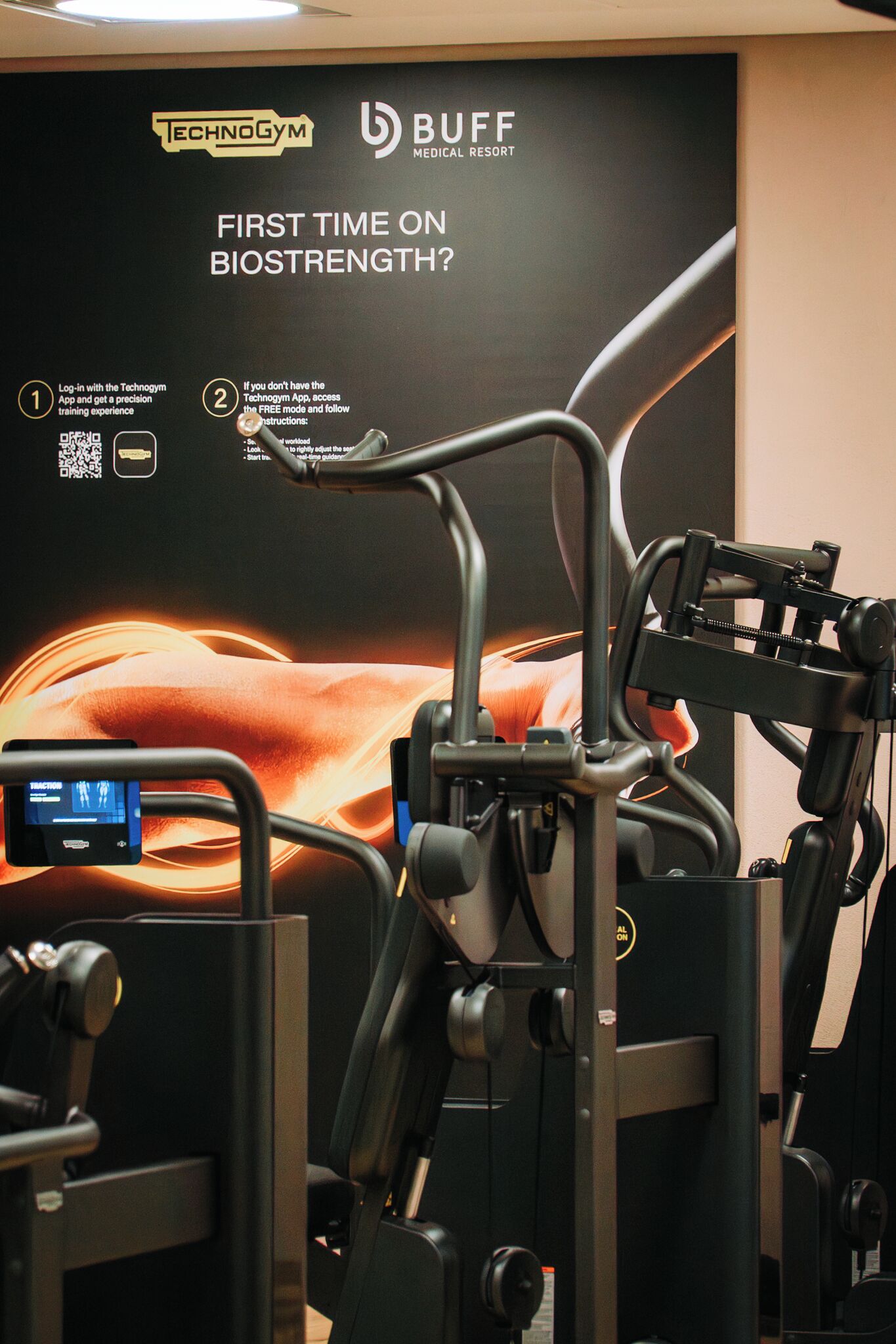 Ein Fitnessgeräte-Arrangement mit einem digitalen Display und einem Plakat, das für ein Biostength-Programm wirbt.