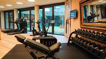 Ein Fitnessstudio mit Cardiogeräten, Kurzhanteln und einer Bank.