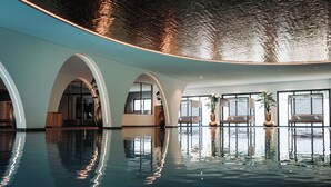 An indoor swimming pool with a reflective surface, arched ceiling, and seating areas with plants.