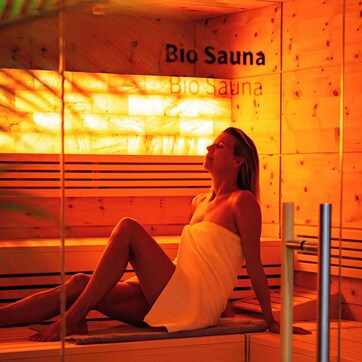 A person in a sauna with wooden walls and a bench, labeled "Bio Sauna".