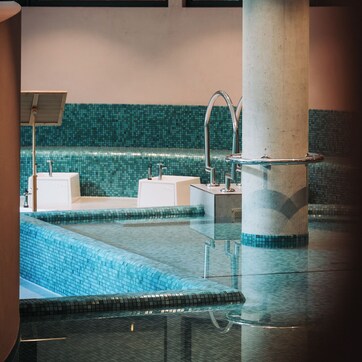 A modern indoor pool area with a clear glass floor, two sinks, and a large pillar.