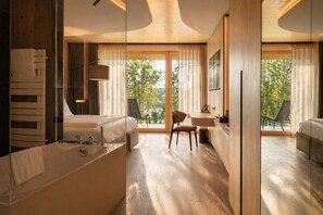 Ein modernes Hotelzimmer mit einer großen Badewanne, einem Bett, einem Schreibtisch und einem Sessel.