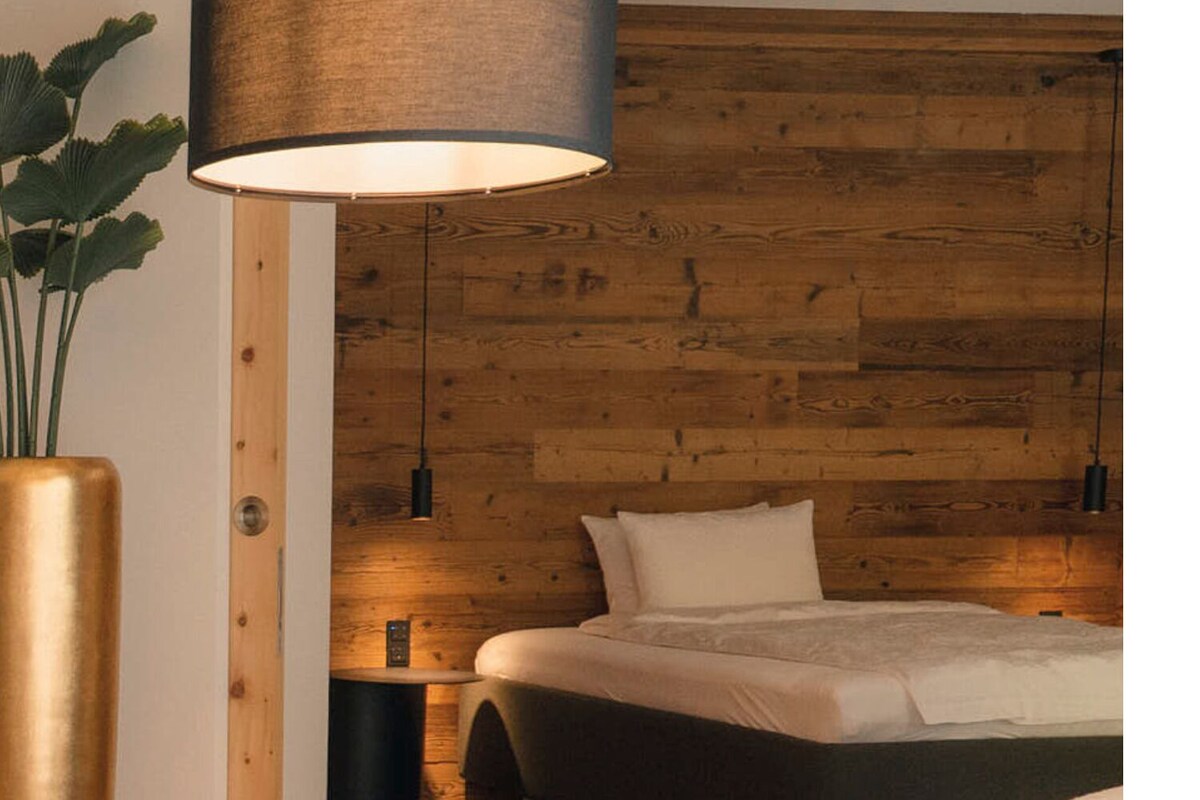 A bedroom with a wooden headboard, a bed, a bedside table, a floor lamp, and a large vase.