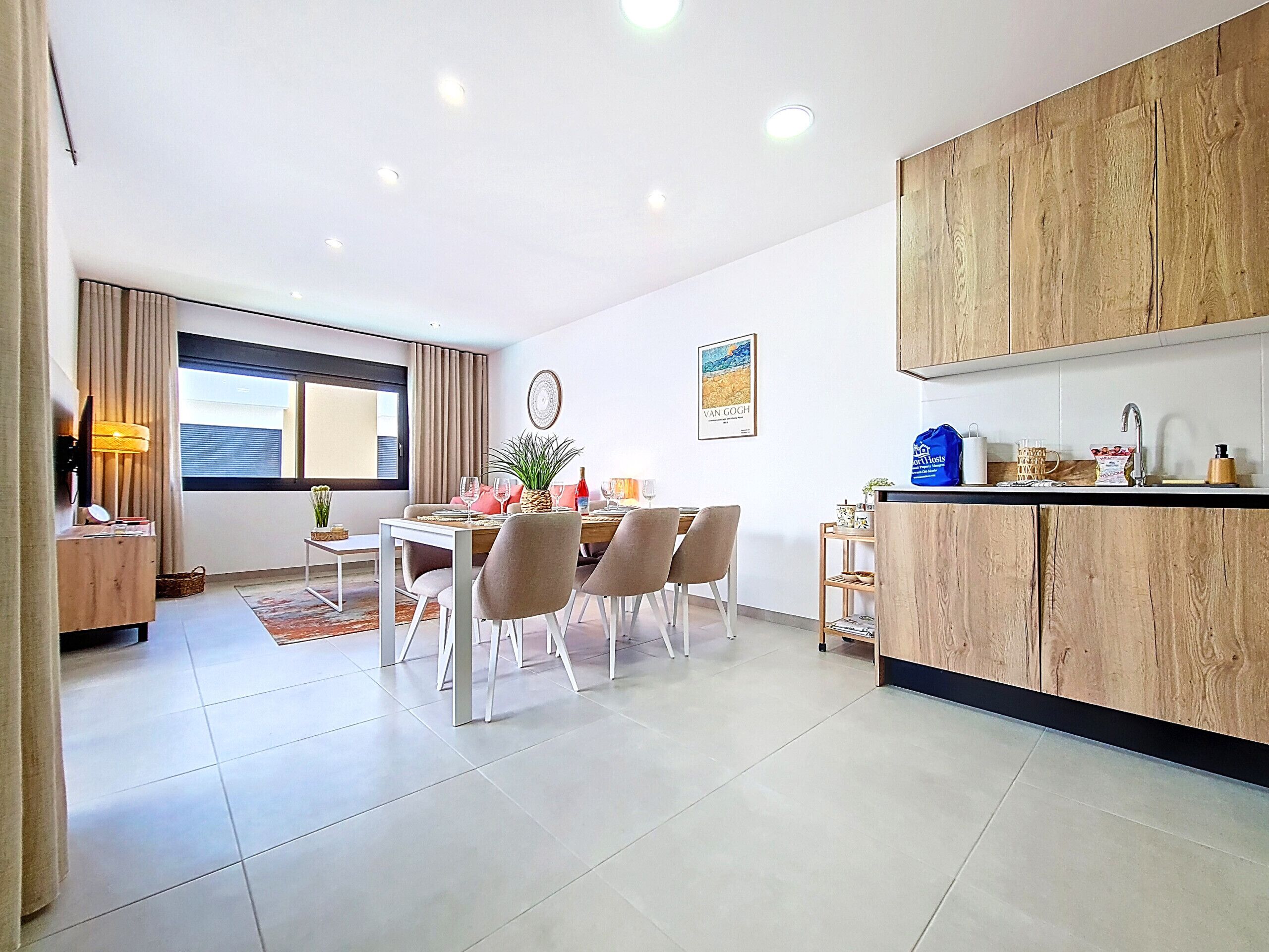 A modern kitchen with wooden cabinets, a dining area with a table and chairs, and a large window with curtains.