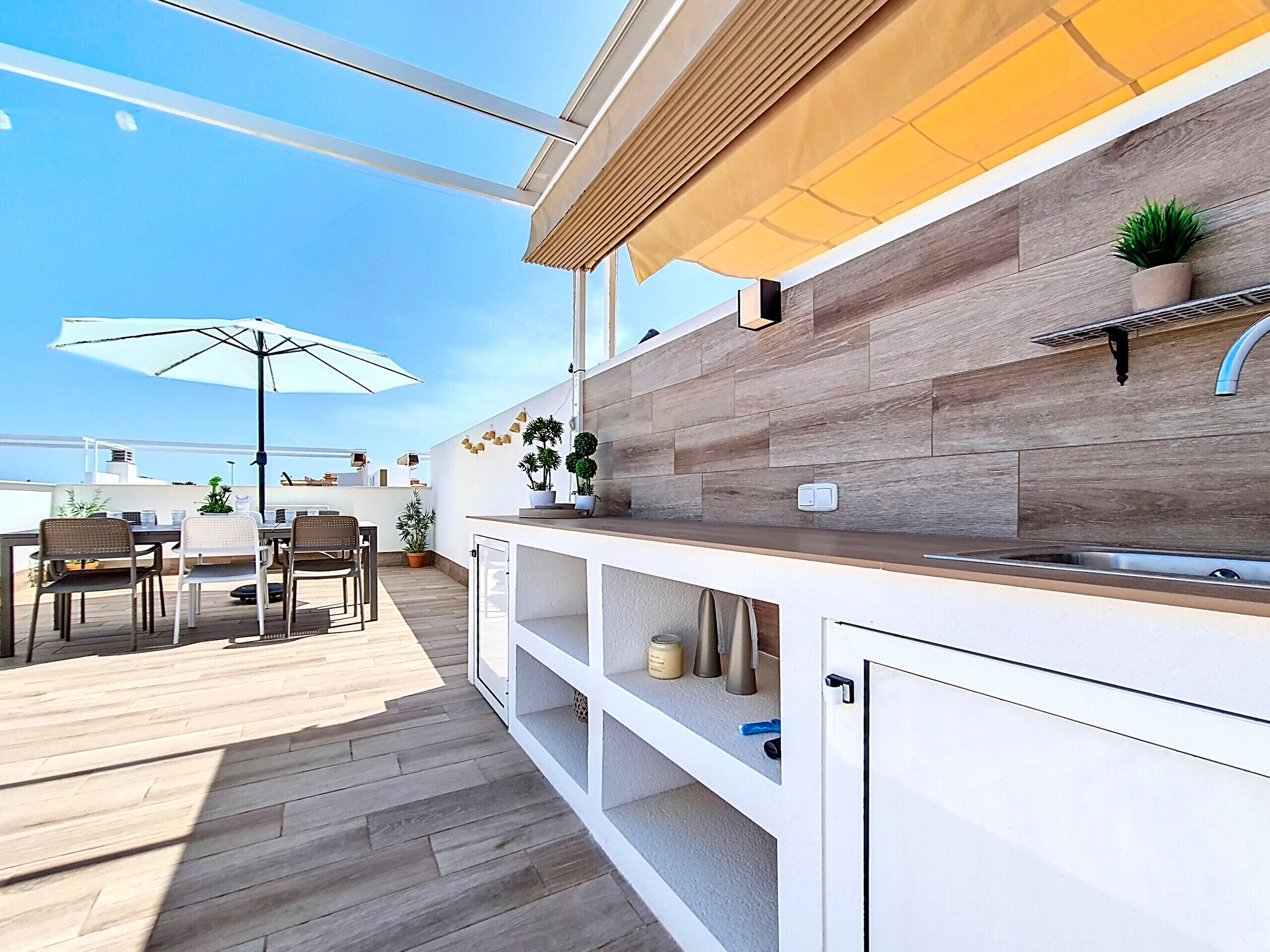 A modern outdoor kitchen area with a wooden countertop, built-in cabinets, and a dining set.