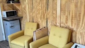 Una habitación con dos sillones amarillos, aire acondicionado blanco, un microondas y una pequeña mesa con un control remoto.
