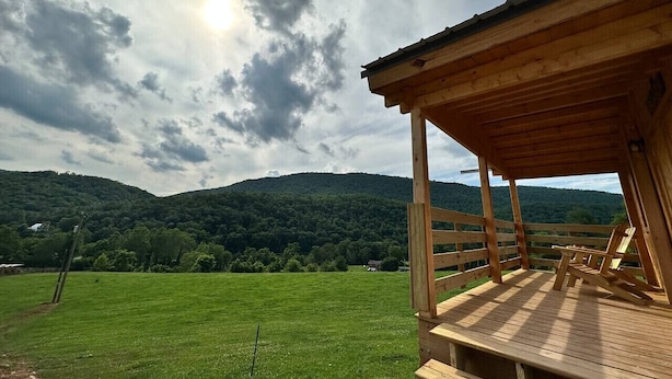 A wooden deck with a view of a green field and mountains.
