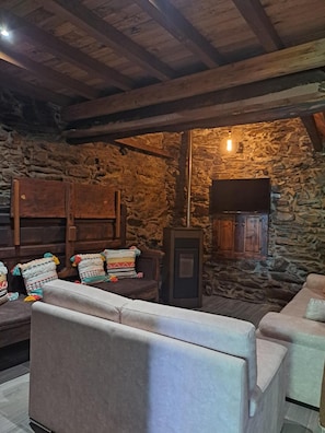 Un intérieur rustique avec des murs en pierre, des poutres en bois, une cheminée et un téléviseur.