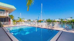 A swimming pool with a clear blue water, surrounded by a white fence, and palm trees in the background. - Anchors Away- Beautiful condo w/ boat slip, boat ramp & Pool (Marathon)