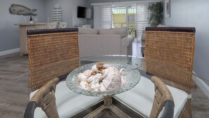 A living room with wicker chairs, a glass table with seashells, a sofa, and a ceiling fan. - Anchors Away- Beautiful condo w/ boat slip, boat ramp & Pool (Marathon)