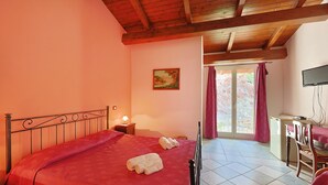 A bedroom with a bed, a desk, a chair, a television, and a window with curtains. - Room 'Filicudi' with Shared Terrace, Shared Garden and Air Conditioning (Patti)