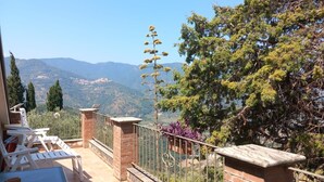 A terrace with a view of mountains, a brick wall, and a metal railing. - Room 'Filicudi' with Shared Terrace, Shared Garden and Air Conditioning (Patti)