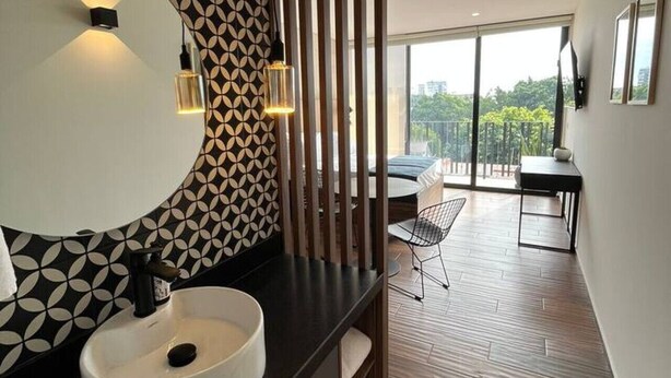 A modern bathroom with a large oval sink, a geometric patterned wall, and a view of a balcony with a dining area.