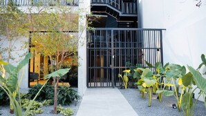 A modern building with a black metal gate, a narrow pathway, and various plants.