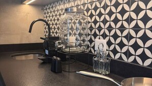 Une cuisine moderne avec un plan de travail noir, une machine à café, un bocal en verre et un crédence décorée.