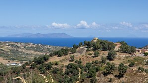 A coastal landscape with scattered buildings, a clear sky, and distant mountains.